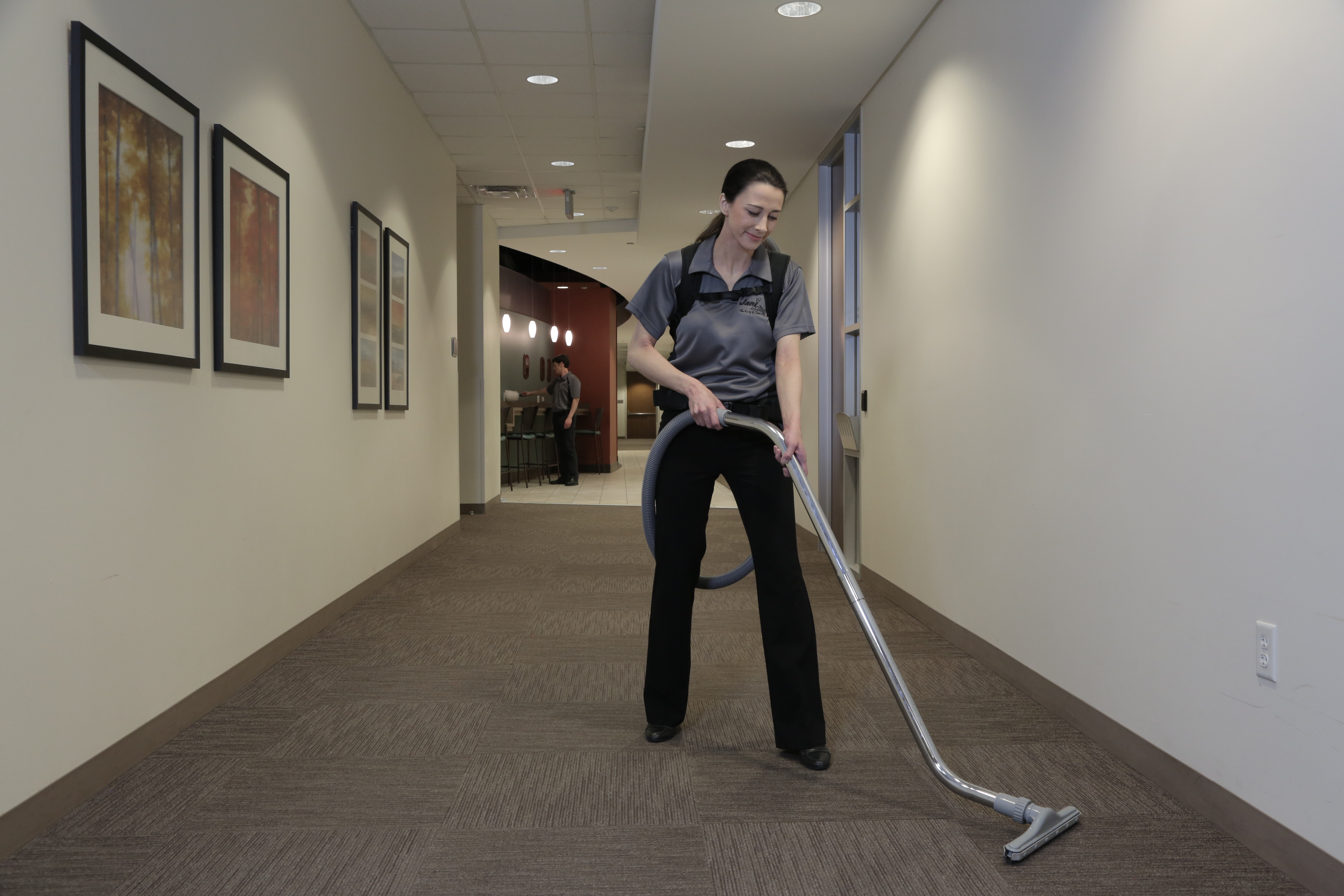 Jani-King commercialc cleaning woman vacuuming carpet in hallway